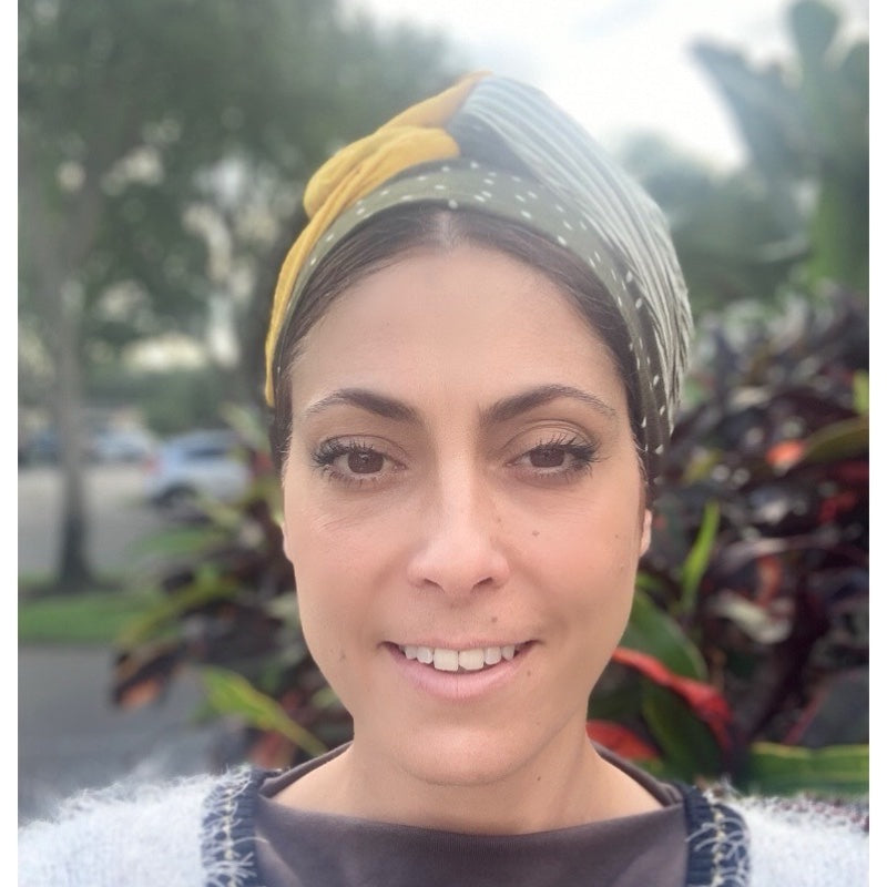 Woman wearing a green and mustard duo tone long scarf headwrap, smiling outdoors