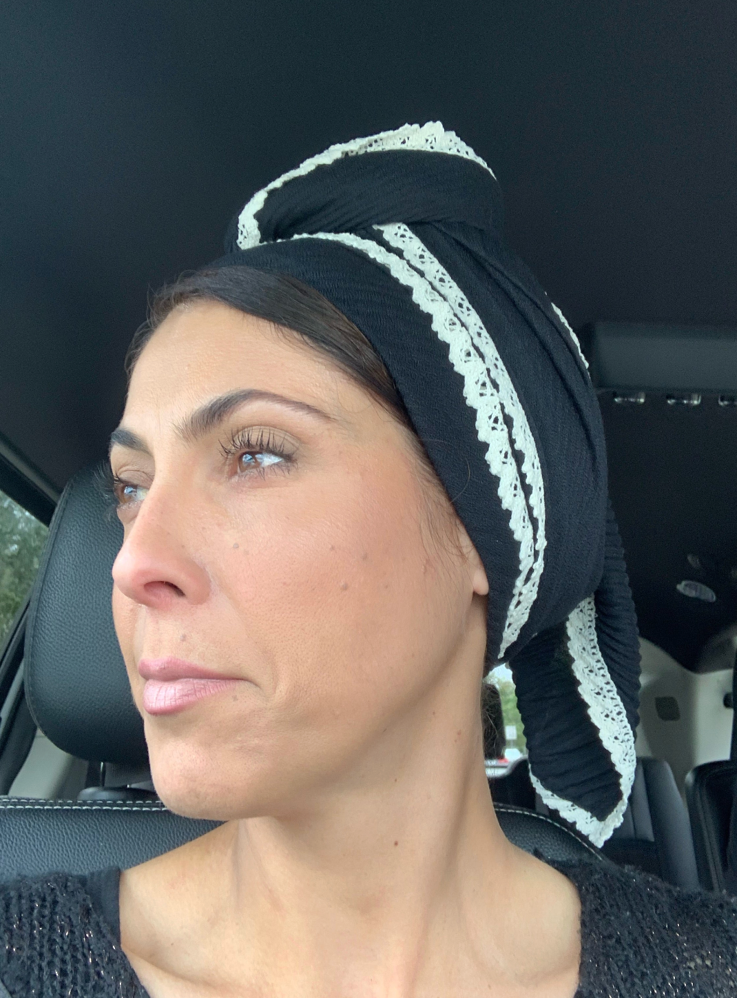 Woman wearing a black pleated long scarf with lace edge wrapped as a headscarf